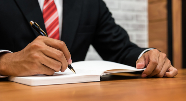 Un hombre con corbata roja escribiendo en un cuaderno