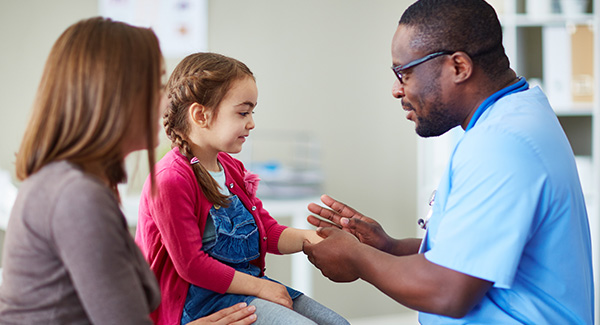 Médico que habla con niña pequeña con su madre al lado