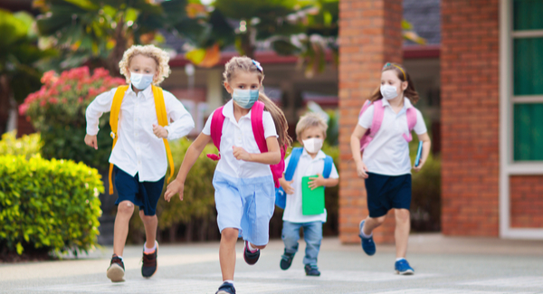 Niños pequeños corriendo al aire libre con barbijos