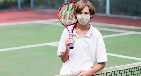 Un niño pequeño jugando al tenis con barbijo