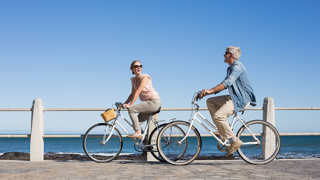pareja de personas mayores andando en bicicleta junto al mar
